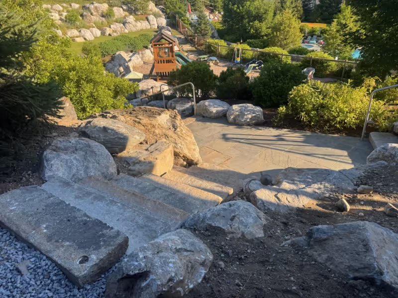 Natural stone steps and large boulders descending through a planted landscape.