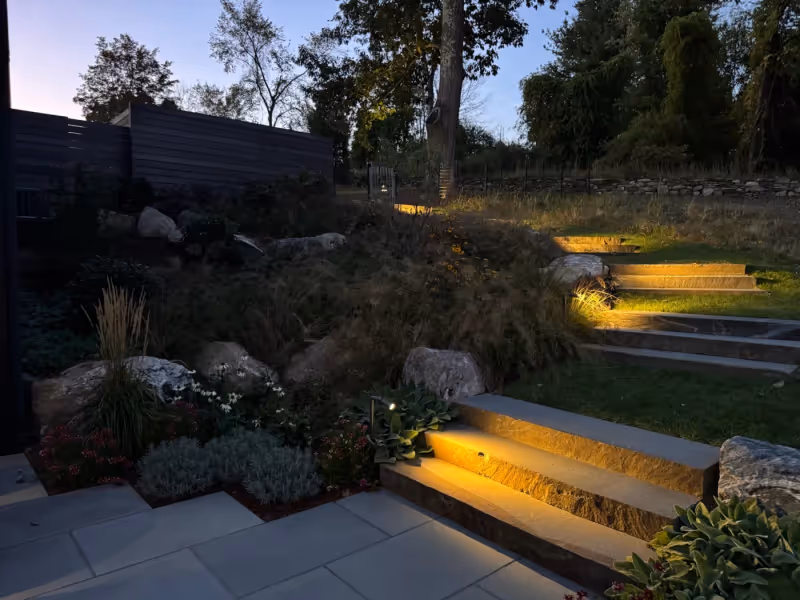 Landscape lighting illuminating stone steps, terrace edges and planting at night.