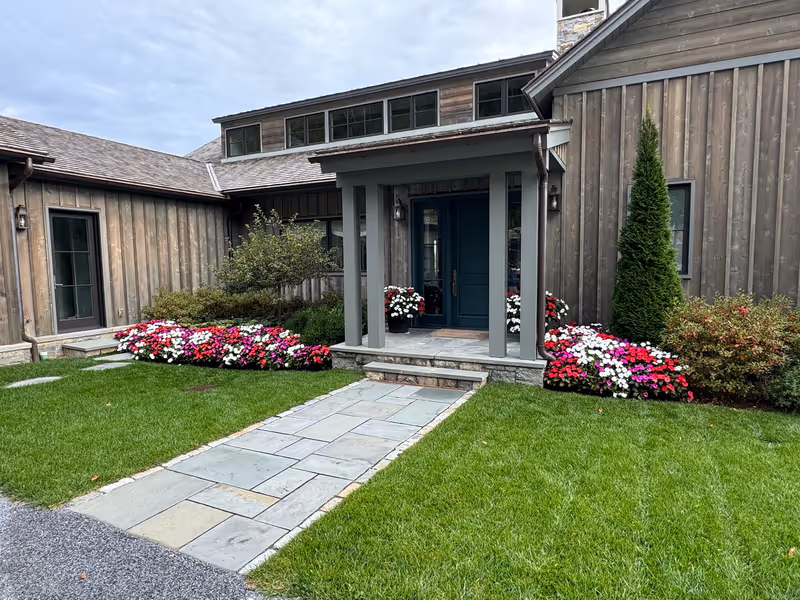 Red and white flowers beside a front entrance, stone walk and lawn.
