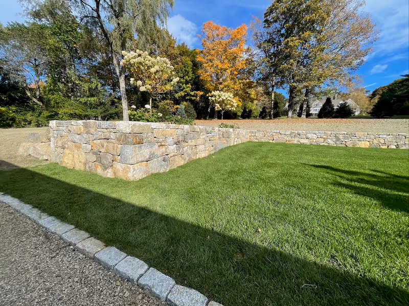 Stone retaining wall bordering a finished lawn with trees and planting above.