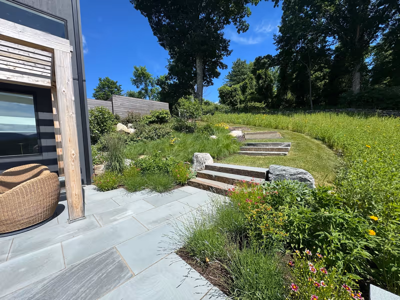 Stone steps ascending a planted slope beside a residential terrace.
