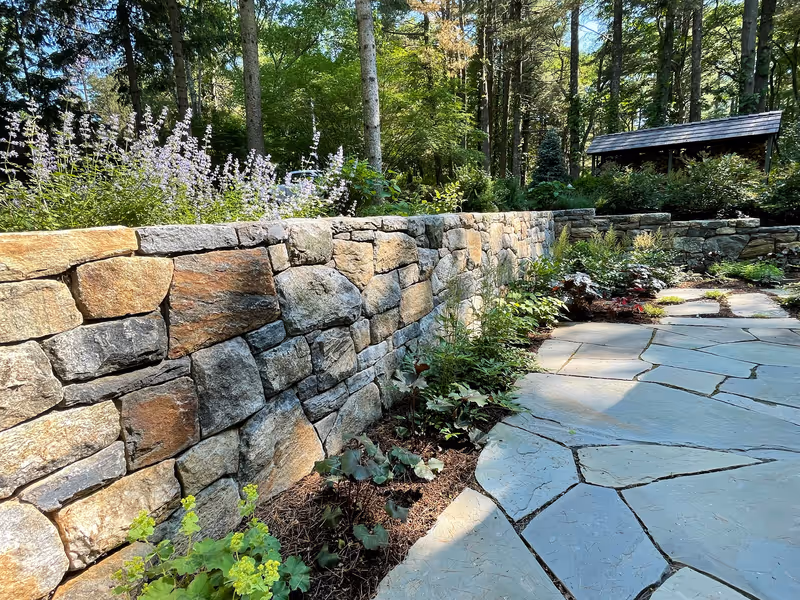 Natural stone wall beside a flagstone walk and flowering garden.