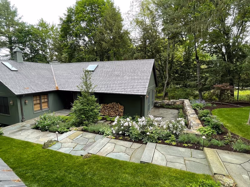 Finished stone paths, steps, planted beds and retaining wall around a wooded residence.